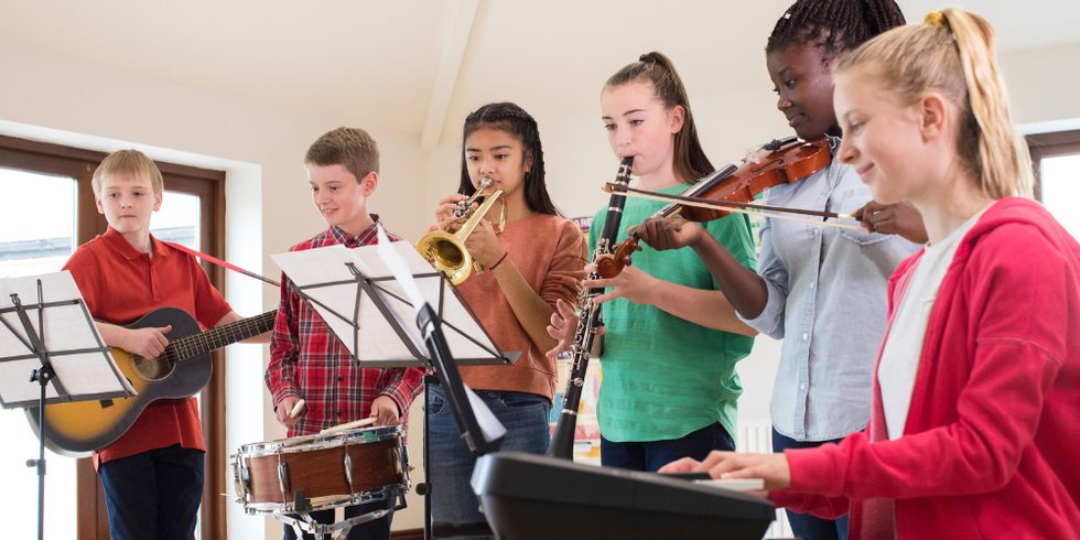 Six students playing together in a home learning space, on guitar, snare drum, trumpet, clarinet, violin and keyboard, reading from music stands