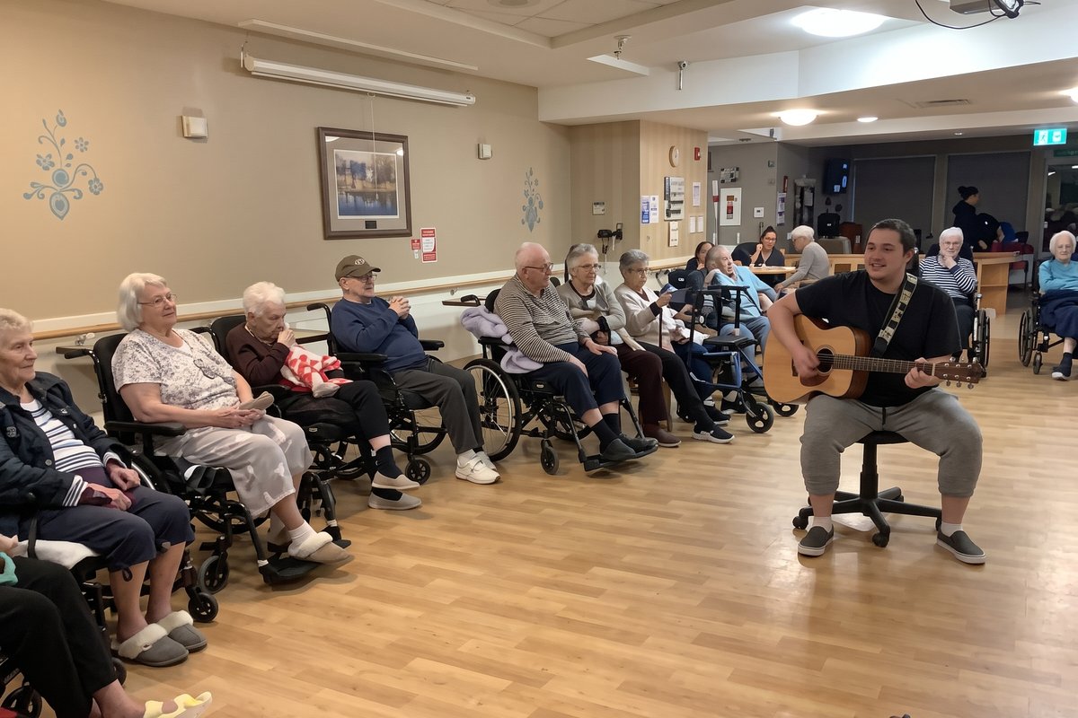 Residents seated in a row in a community room listening to a musician playing acoustic guitar